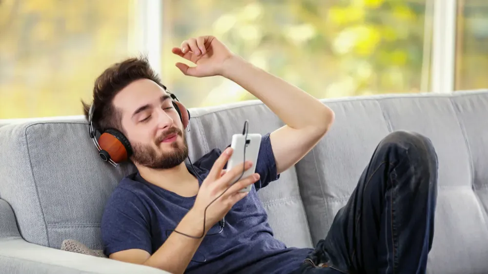 man listening to heapdphones on grey sofa